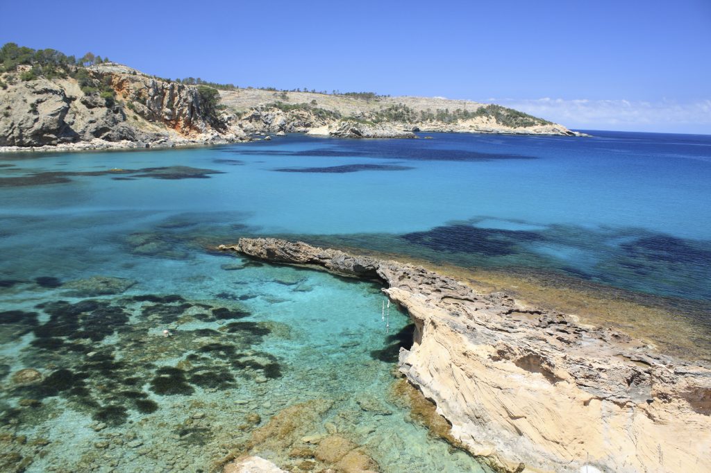 Cala Xarraca beach in Ibiza with clear blue water and rocky coastline